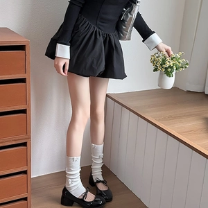 Detail of a short black dress with pleated skirt and white bow stockings in a warm room