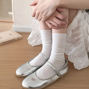 Silver mirror Mary Jane flats with white ribbed crew socks on a light wood floor