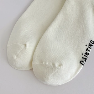 Close-up of white cotton crew socks with DAINTING letter print and fine knit texture