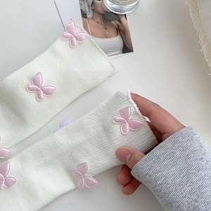 Detailed close-up of white ribbed knit leg warmers with 3D pink butterfly appliques