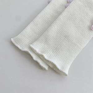 Detail of cream rib-knit leg warmer with purple flower patch and ruffled edges