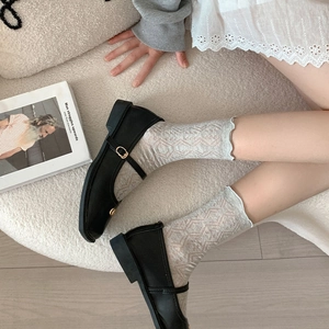Dettaglio di calze a rete grigio chiaro con bordo in pizzo abbinate a scarpe Mary Jane
