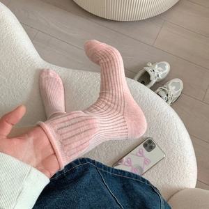 Gros plan de chaussettes en coton côtelé rose à bords roulés dans un décor de vie chaleureux
