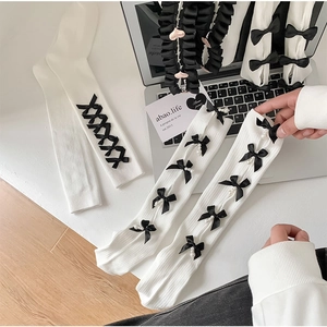 Detail of white rib-knit balletcore leg warmers with black bows and pearl accents