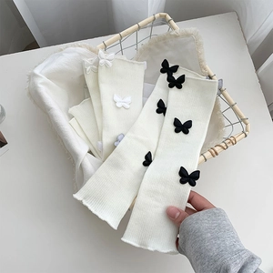 Detailed view of white ribbed leg warmers featuring 3D bow appliques in a basket