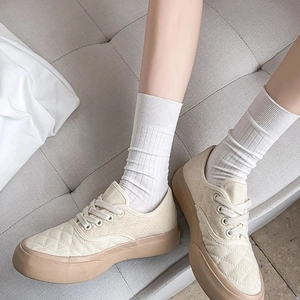 Close-up of beige quilted sneakers with thick gum sole and white mid-calf knit socks