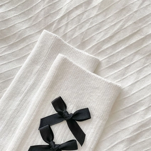 Detail of white ribbed knit calf socks with a black silk bow decoration on the top