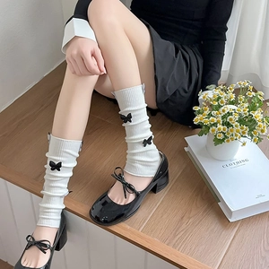 Close-up of white knitted leg warmers with black 3D bows paired with Mary Jane shoes