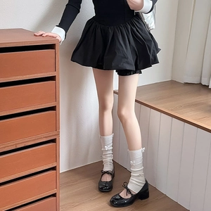 Close-up of white ribbed leg warmers with bows and black Mary Jane shoes in balletcore style