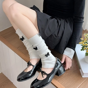 Detailed view of white ribbed knit leg warmers with black 3D bows on Mary Jane shoes