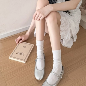 Detail of white ribbed crew socks paired with silver Mary Jane shoes on wood floor