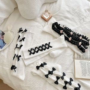 Detail of JK Lolita socks with bows and pearls displayed on white striped sheets