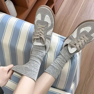 Detail of grey ribbed crew socks paired with vintage sneakers on a blue striped sofa