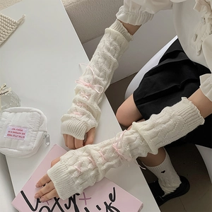Close-up of cable knit cream arm warmers with decorative pink cross-tie ribbons