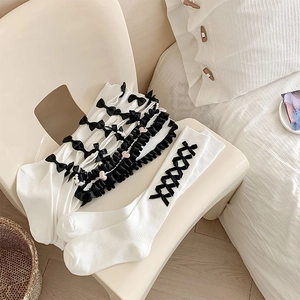 Detailed view of Lolita knee-high socks with lace trim, bows, and pearls in black and white