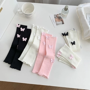 Detail of knit leg warmers with ribbon bows and wavy edges in black, white, and pink