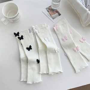 Flat lay of white knit leg warmers with 3D colorful butterfly patches and chic props