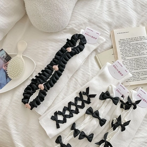 Detailed view of white Lolita socks with black lace, bows and pearls on a white fabric