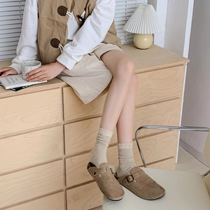 Detail of brown suede clogs with metal buckle and beige textured knit crew socks