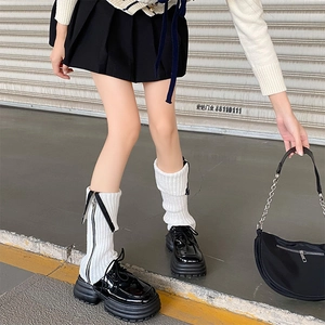 Detail of white ribbed knit leg warmers with side zipper styled with black loafers
