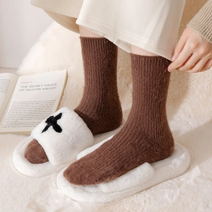 Thick brown cable knit socks for winter paired with plush slippers on a cozy rug