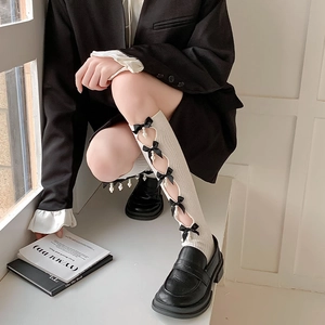 Detail of white ribbed knee-high socks with black silk bows and dangling pearls