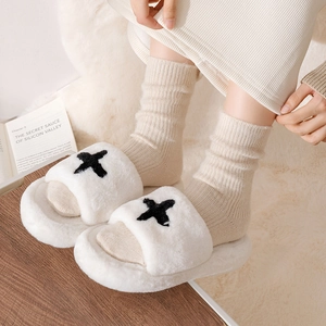 Close-up of white plush slippers with black cross-stitch pattern and thick warm socks