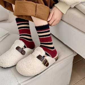 Gros plan de sabots en fausse fourrure blanche avec chaussettes rayées rouges et noires