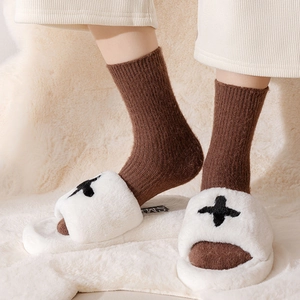 Close-up of soft white plush slippers with cross embroidery and thick thermal cotton socks