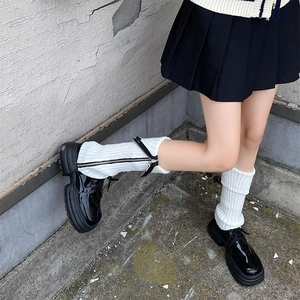 Detail of white ribbed knit leg warmers with side zippers paired with black patent leather shoes