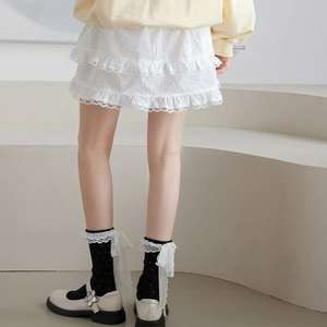 Détail de chaussettes résille noires à pois avec nœuds en dentelle blanche et volant