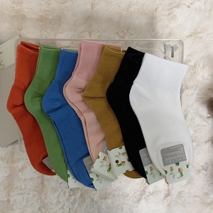 Colorful cotton mid-calf socks in seven vibrant shades displayed on a plush white surface
