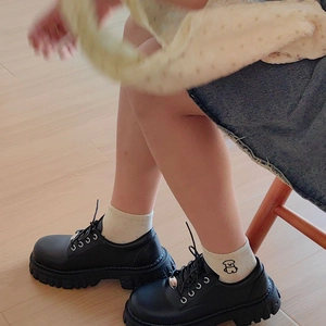 Detail of cream knit crew socks with cute cartoon embroidery paired with black loafers