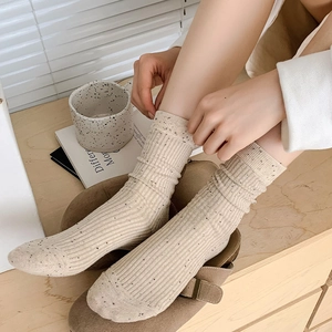Detail of cream rib-knit crew socks with black speckles shown in a cozy lifestyle setting