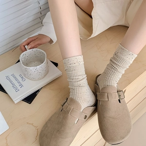 Detail of khaki suede clogs paired with cream dotted knit mid-calf socks for a cozy look
