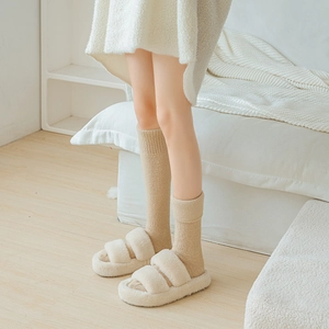 Detailansicht der cremeweißen Plüschhausschuhe und dicken khakifarbenen Thermo-Socken