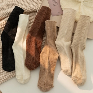 Set of 6 thick knit crew socks in earthy tones laid on a cozy winter blanket background