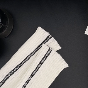 Detail of white ribbed knit leg warmer with a black side zipper on leather background