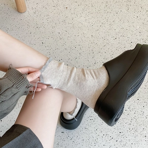 Close-up of beige ribbed crew socks paired with black platform mule slides on pavement