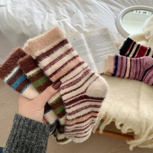 Gros plan de chaussettes pelucheuses à rayures colorées sur un fond de literie douillet