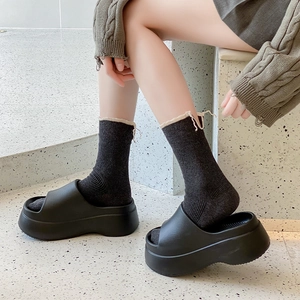 Women's black platform slide sandals styled with wavy-edge crew socks on stone ground