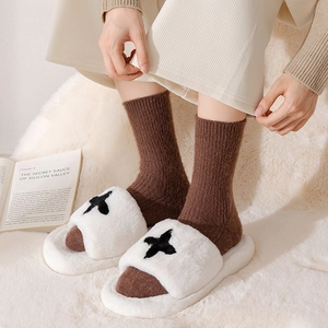 Detail of white plush slippers with cross pattern and brown knitted thermal socks