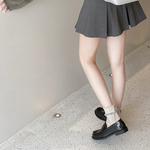 Close-up of beige knitted mid-calf socks styled with black loafers and a grey pleated skirt