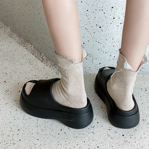 Close-up of black EVA platform slides worn with beige ribbed mid-tube socks and frayed edges