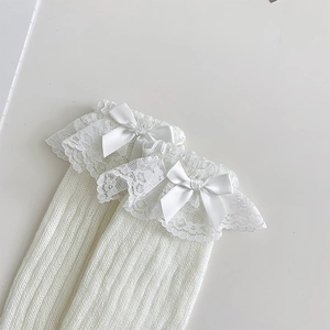 Detail von weißen Beinstulpen mit zartem Spitzenbesatz und Satin-Schleifen