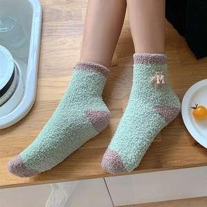Close-up of green and pink coral fleece socks featuring a cute 3D bear patch detail