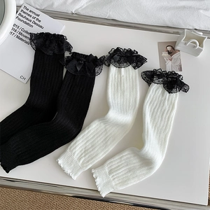 Detail von weißen und schwarzen Strickbeinstulpen mit Spitzenbesatz und Satinschleifen