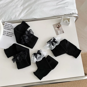 Detail von schwarzen Strickbeinstulpen mit Spitzenbesatz und Bandschleifen auf weißem Tisch