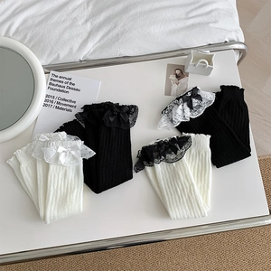 Detailansicht gestrickter Stulpen mit Spitzenbesatz und Schleifen in Weiß und Schwarz