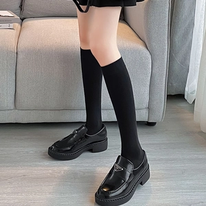 Detail of black glossy platform loafers with metal triangle logo and knee-high socks